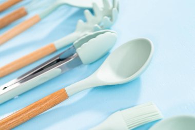 Mavi arka planda ahşap saplı yeni mavi silikon mutfak aletleri..