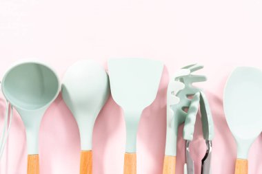 Pembe arka planda ahşap saplı yeni mavi silikon mutfak aletleri..