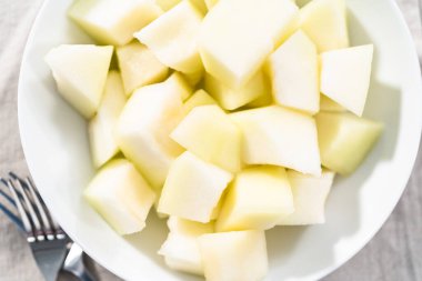 Beyaz bir kasede dilimlenmiş altın çiğ taneli kavun..