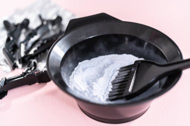 Siyah plastik bir kasede pembe arka planda saç boyası tozu..