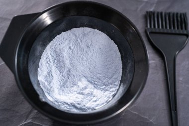 Siyah arka planda siyah plastik bir kasede saç boyası tozu..