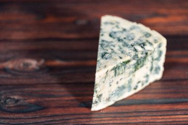 Koyu ahşap arka planda büyük bir dilim mavi peynir..