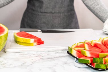 Beyaz bir kesme tahtasının üzerinde çekirdeksiz kırmızı karpuz dilimliyorum..