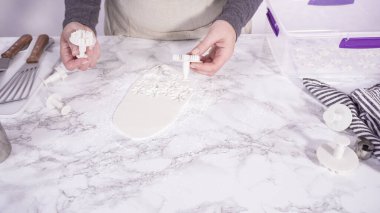 Adım adım. Mermer tezgahın üzerindeki beyaz fondanla kar tanelerini keserek..