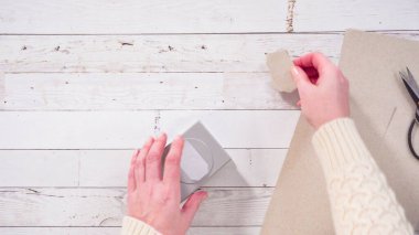 Düz yatıyordu. Adım adım. Kahverengi kağıttan hediye etiketlerini kağıt punçla kesiyor..