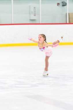 Küçük kız buz pateni pistinde artistik patinaj yapıyor..