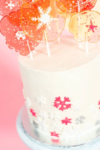 又高又圆的蛋糕 上面有意大利奶油霜 上面装饰着可爱的雪花 粉红的背景上有大大的粉色和白色棒棒糖 — 图库照片
