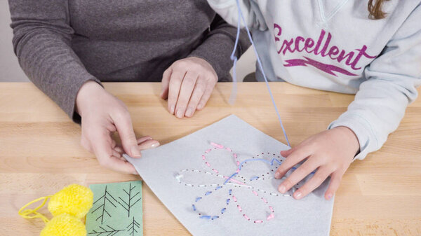 Маленькая девочка учится шить со своей матерью за рабочим столом.