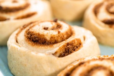 Fırınlanmamış tarçınlı çörekler mavi bir tavada.