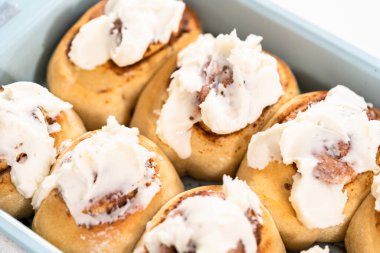 Taze pişmiş tarçınlı rulo, beyaz kremalı, mavi bir tavada..