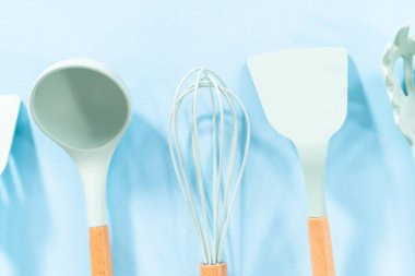 Mavi arka planda ahşap saplı yeni mavi silikon mutfak aletleri..