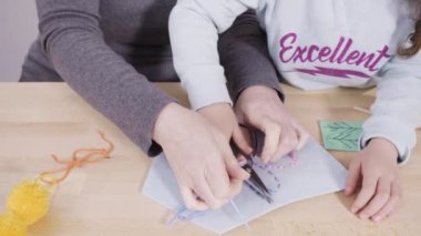 Küçük kız annesiyle el sanatları masasında dikiş dikmeyi öğreniyor..