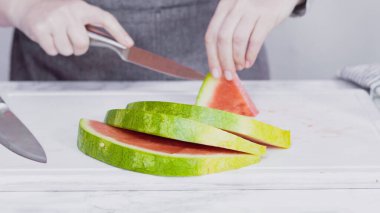 Kırmızı karpuzu beyaz bir kesme tahtasının üzerinde küçük parçalara ayırmak.