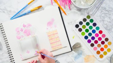 Düz yatıyordu. Baker suluboyalı bir doğum günü pastası çiziyor..