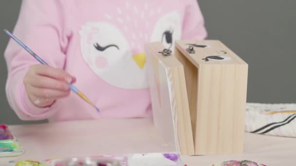 小さな女の子は木製の箱の上にアクリル絵具で白いユニコーンを描く — ストック動画