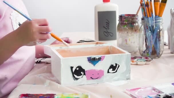 小女孩在木箱上画了一只白色独角兽 上面涂着丙烯酸颜料 — 图库视频影像
