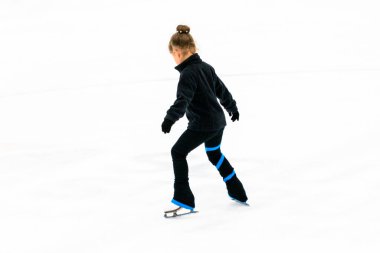 Siyah elbiseli küçük artistik patinajcı, kapalı buz arenasında pratik yapıyor..