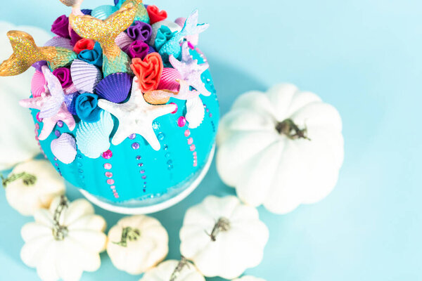 Halloween craft pumpkins decorated with mermaid tails, glitter, and sparkly rhinestones on a blue background.