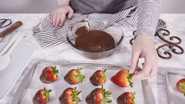 Adım adım. Çikolata kaplı çilek hazırlamak için organik çilekleri erimiş çikolatayla bir kaseye daldırmak..