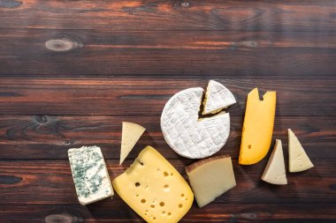 Flat lay. Variety of large gourmet cheese wedges on a dark wooden background. clipart
