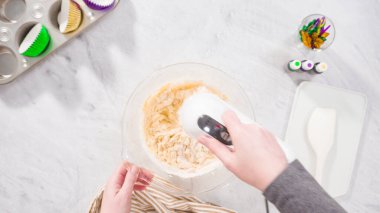 Düz yatıyordu. Adım adım. Vanilyalı Mardi Gras kekleri pişirmek için karışımı elektrikli mikserle karıştırıyorum..