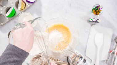 Düz yatıyordu. Adım adım. Vanilyalı Mardi Gras kekleri pişirmek için karışımı elektrikli mikserle karıştırıyorum..