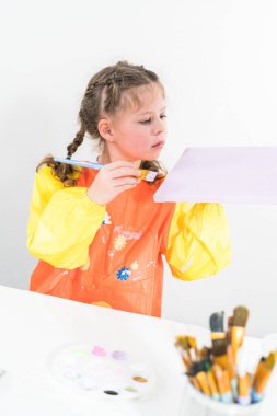 Evde akrilik boyalı bir sanat projesi üzerinde çalışan küçük bir kız..