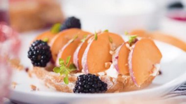 Beyaz tabakta böğürtlenlerle süslenmiş şeftalili ricotta tostu.