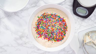 Düz yatıyordu. Adım adım. Pasta hamurunun içine renkli şekerlemeler serpiştirip funfetti keki yapıyorum..