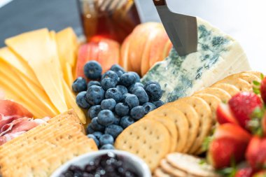 Aperatif olarak sunulan tahtanın üzerinde gurme peyniri, kraker ve meyve var..