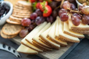 Gourmet cheese, crackers, and fruit on a wood cutting board served as an appetizer. clipart