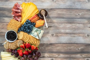 Düz yatıyordu. Aperatif olarak sunulan tahtanın üzerinde gurme peyniri, kraker ve meyve var..