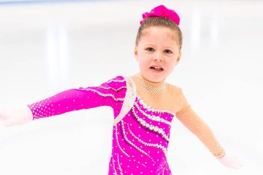 Pembe elbiseli küçük artistik patinajcı kapalı buz pistinde pratik yapıyor..