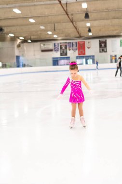 Pembe elbiseli küçük artistik patinajcı kapalı buz pistinde pratik yapıyor..