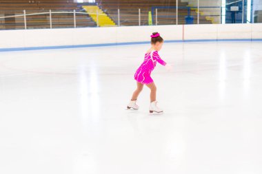 Pembe elbiseli küçük artistik patinajcı kapalı buz pistinde pratik yapıyor..