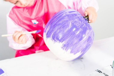 Küçük kız mor akrilik boyayla balkabağı boyuyor..