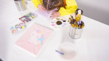 Uzak bir sanat projesi için annesiyle tuvale akrilik boyayla resim yapan küçük bir kız..