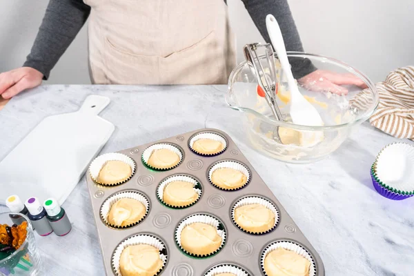 Vanilla cupcake batter in foil cupcake liners to bake Mardi Gras vanilla cupcakes.