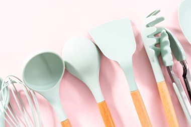 Pembe arka planda ahşap saplı yeni mavi silikon mutfak aletleri..