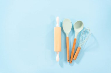 Düz yatıyordu. Mavi arka planda ahşap saplı yeni mavi silikon mutfak aletleri..