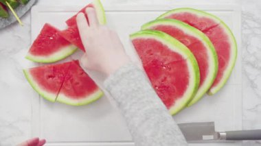 Düz yatıyordu. Kırmızı karpuzu beyaz bir kesme tahtasının üzerinde küçük parçalara ayırmak.