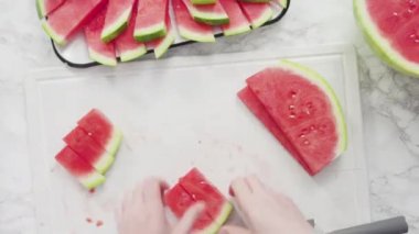 Düz yatıyordu. Kırmızı karpuzu beyaz bir kesme tahtasının üzerinde küçük parçalara ayırmak.