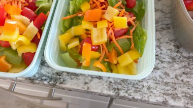 Mutfak tezgahında yeniden kullanılabilir yiyecek kapları romaine marul, kiraz domatesleri, doğranmış havuçlar ve doğranmış biberlerle doludur. Kurulum sağlıklı yeme alışkanlıklarını yansıtıyor..