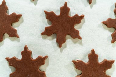 Çiğ çikolatalı, zencefilli, kar tanesi şekilli kurabiyelerin parşömen astarlı fırın tepsisine yerleştirilmiş, pişirmeye hazır..