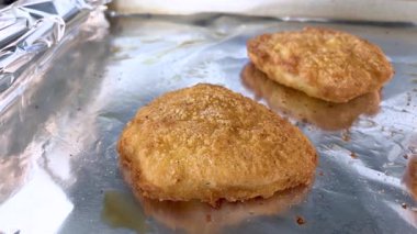 Fırından yeni çıkmış iki fırında pişmiş altın sarısı hamur işi folyo tepsisinin üzerinde duruyor. Işıklandırma, yumuşak yüzeylerini ve çıtır çıtır kenarlarını vurguluyor..