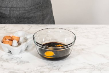 Klasik zencefilli kurabiye hamuru, pekmez, eritilmiş tereyağı ve yumurta içeren ıslak malzemeler içeren cam kasenin göz hizasında görüntüsü. Bir çırpı kabın içinde, malzemeleri karıştırmaya hazır.