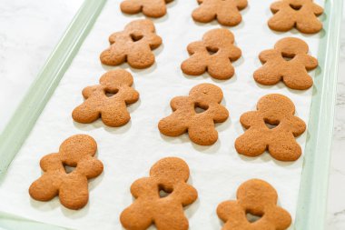 Parşömen kağıdında kalp şeklinde kesikler olan fırınlanmış zencefilli kurabiye adam kurabiyelerinin açılı görüntüsü.