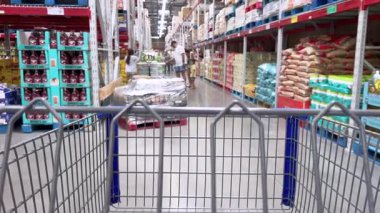 Parker, Colorado, ABD-20 Haziran 2025 Slow Motion, depo koridorunda bir alışveriş arabasını iten birinin görüntüsü. Toplu ürünler uzun raflarda yığılmıştır..