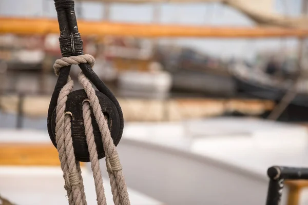 Polea para velas y cuerdas de madera en un viejo velero, con vela y otros barcos fuera de foco en el fondo . — Foto de Stock