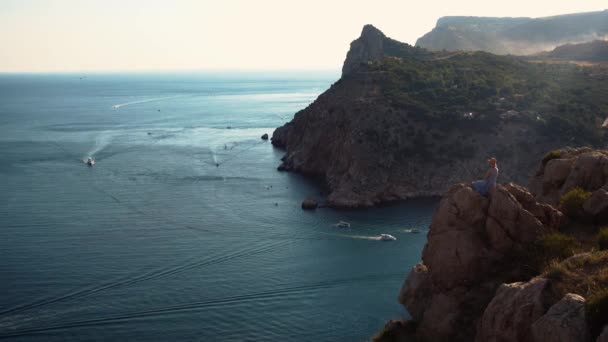 Mädchen sitzt auf dem Felsen und blickt auf die schöne Aussicht auf das Meer mit Booten — Stockvideo